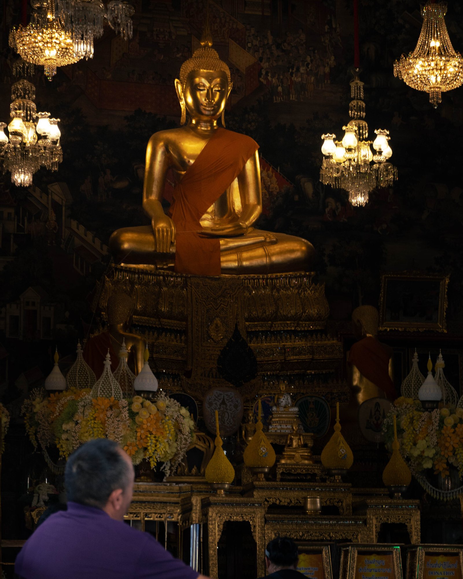 Posąg Buddy na tle ciemnych malowideł ściennych w Wat Arun w Bangkoku.