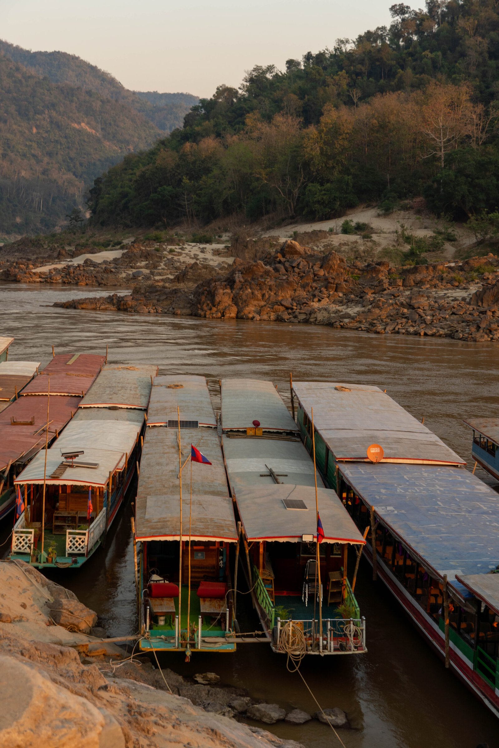 Slow boat na Laosie płynący po rzece Mekong o zachodzie słońca, malowniczy krajobraz podróży po Azji Południowo-Wschodniej