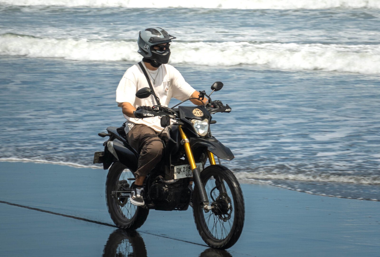 Mężczyzna na skuterze jadący po plaży z czarnym piaskiem z widokiem na ocean na Bali, Indonezja