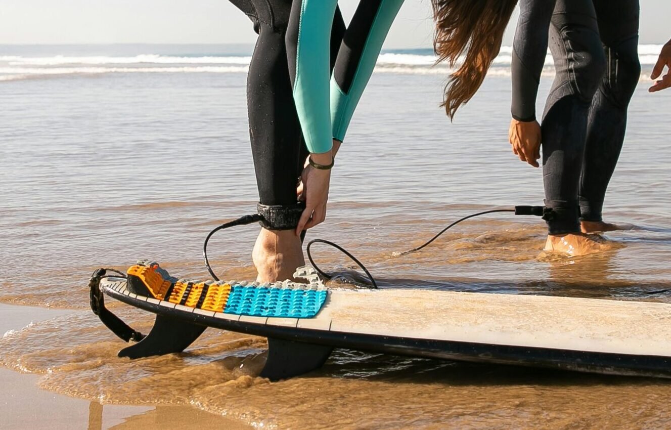 Two surfers in wetsuits preparing their boards on a sunny Portugal beach.