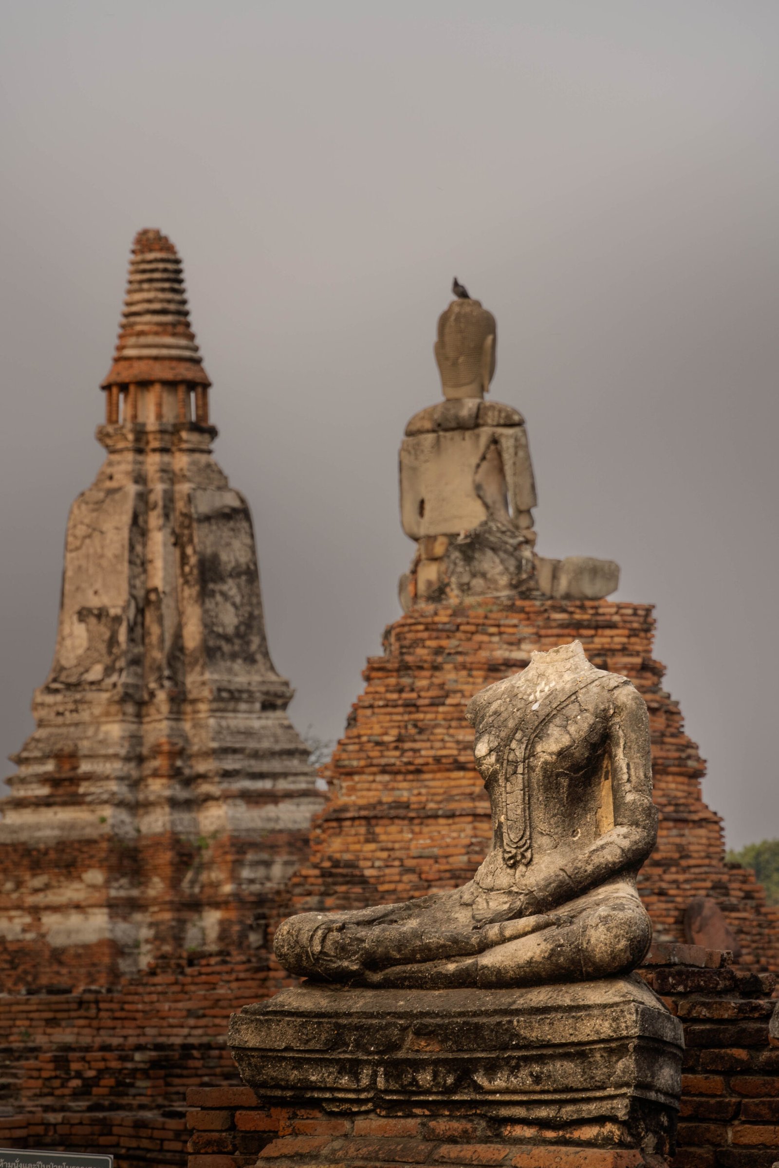 Posąg Buddy bez głowy w ruinach świątyni Wat Chaiwatthanaram w Historycznym Parku Ayutthaya (Tajlandia). Zdjęcie przedstawia zniszczony, ale majestatyczny zabytek Tajlandii, podkreślający historię i dziedzictwo Ayutthayi