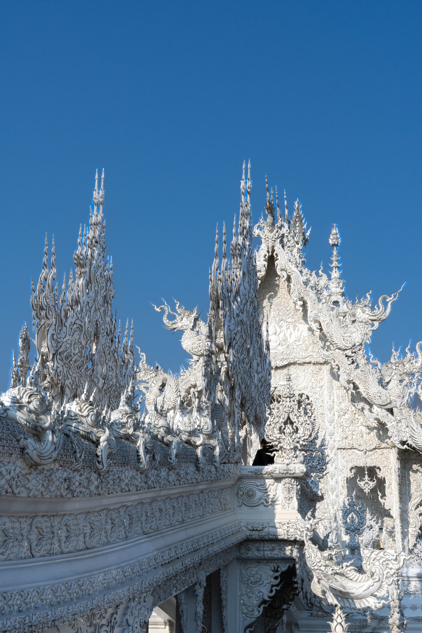 Biała Świątynia (Wat Rong Khun) w Chiang Rai, lśniąca w słońcu. Zdjęcie przedstawia nietypową, współczesną architekturę tajską, dekorowaną mozaiką ze szkła i charakteryzującą się mostem reinkarnacji nad stawem.