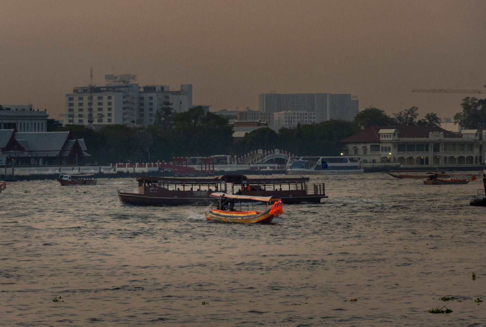 Porównanie łodzi na rzece Chao Phraya w Bangkoku: tradycyjna łódź longtail i statek pasażerski podczas zachodu słońca