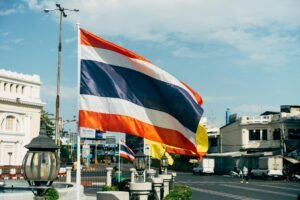 Street scene with Thailand's flag waving prominently on a clear day.